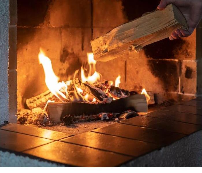 a person laying another wood log into hot burning fireplace